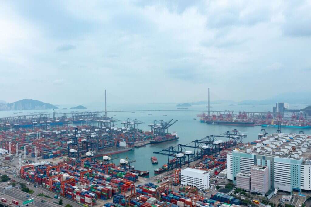 Aerial view of a container port with stacked shipping containers and quay cranes