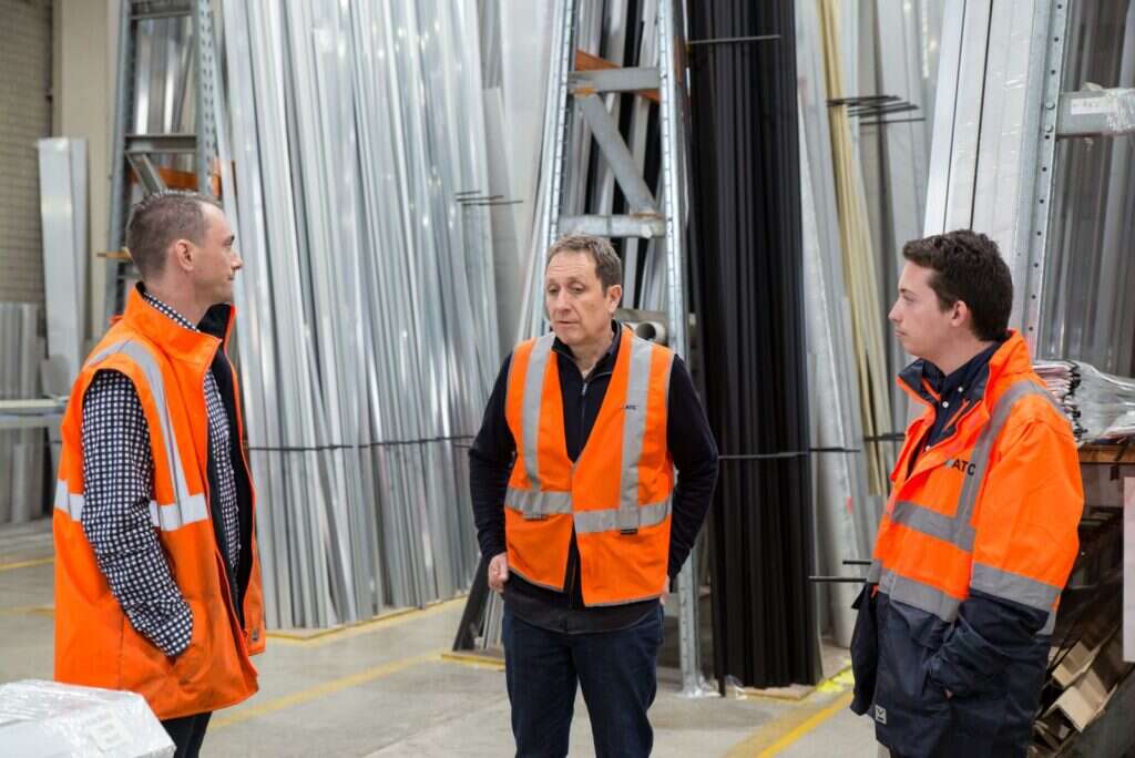 Team members in high-visibility vests talking inside a metal warehouse