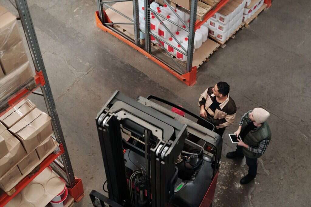 Two warehouse workers coordinating logistics near a forklift, viewed from above