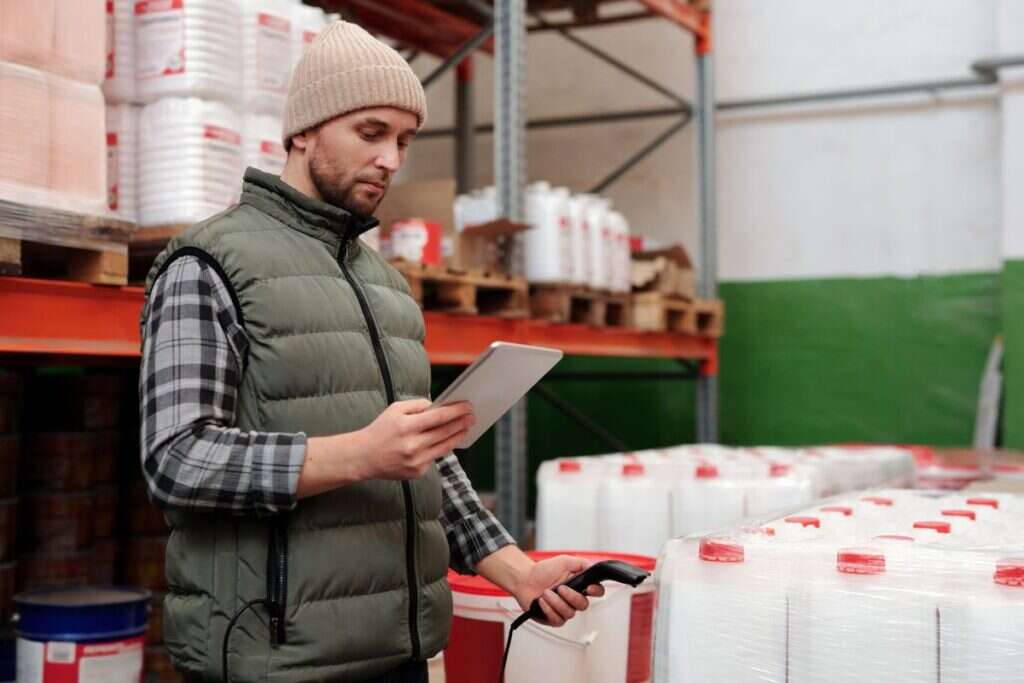 Warehouse operative managing stock inventory on a tablet beside storage racking